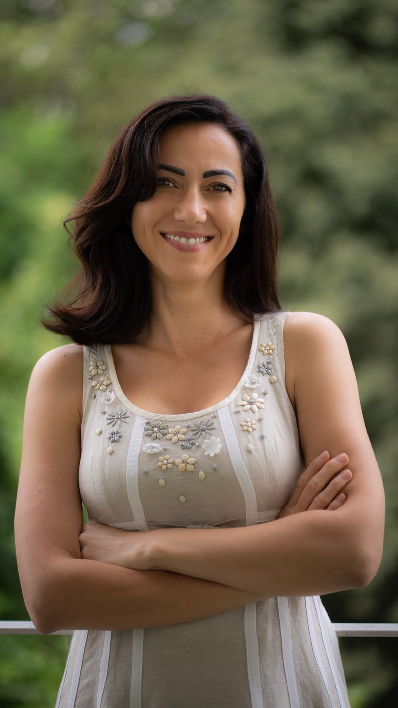 Dra. Clara Furtenzi, dermatologista, de braços cruzados ao ar livre, sorrindo